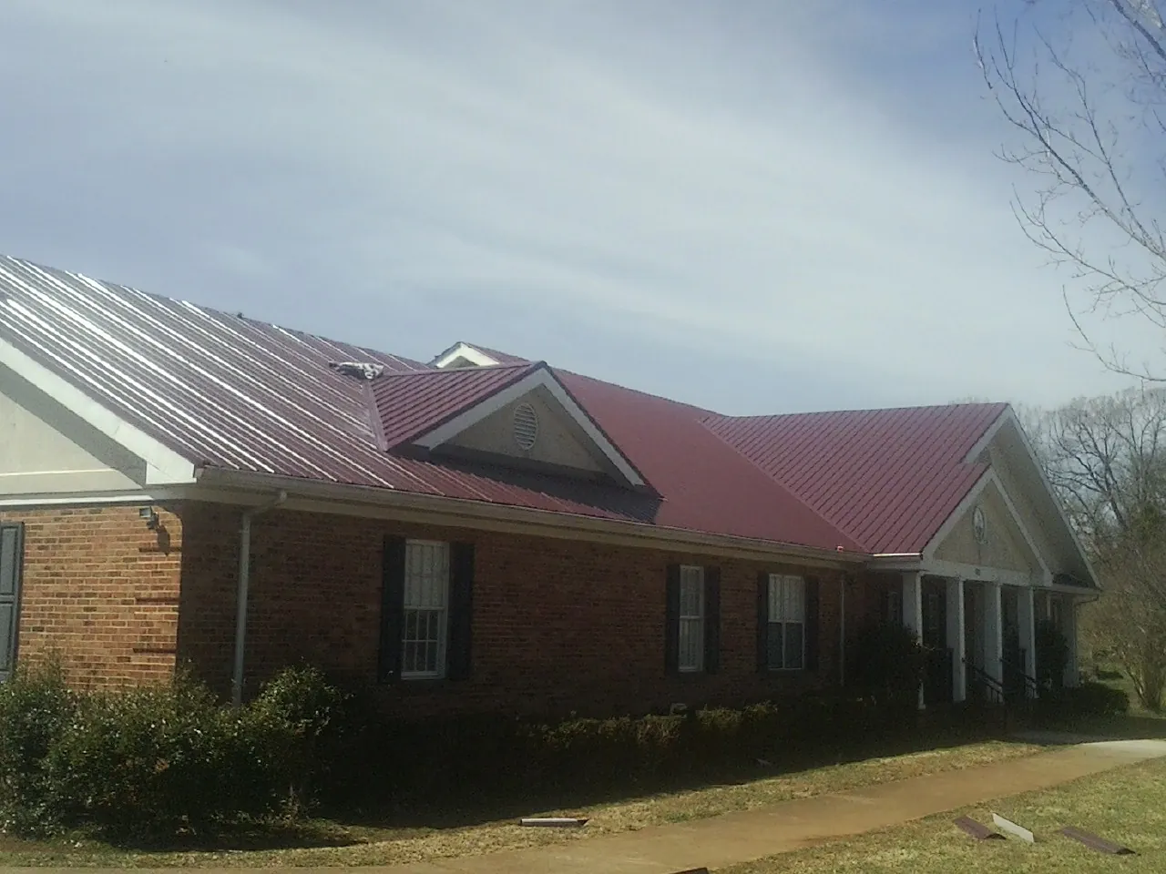 Red metal roof with gabled entries on a long brick building, from a Hail Damage Roof Repair job in Warminster