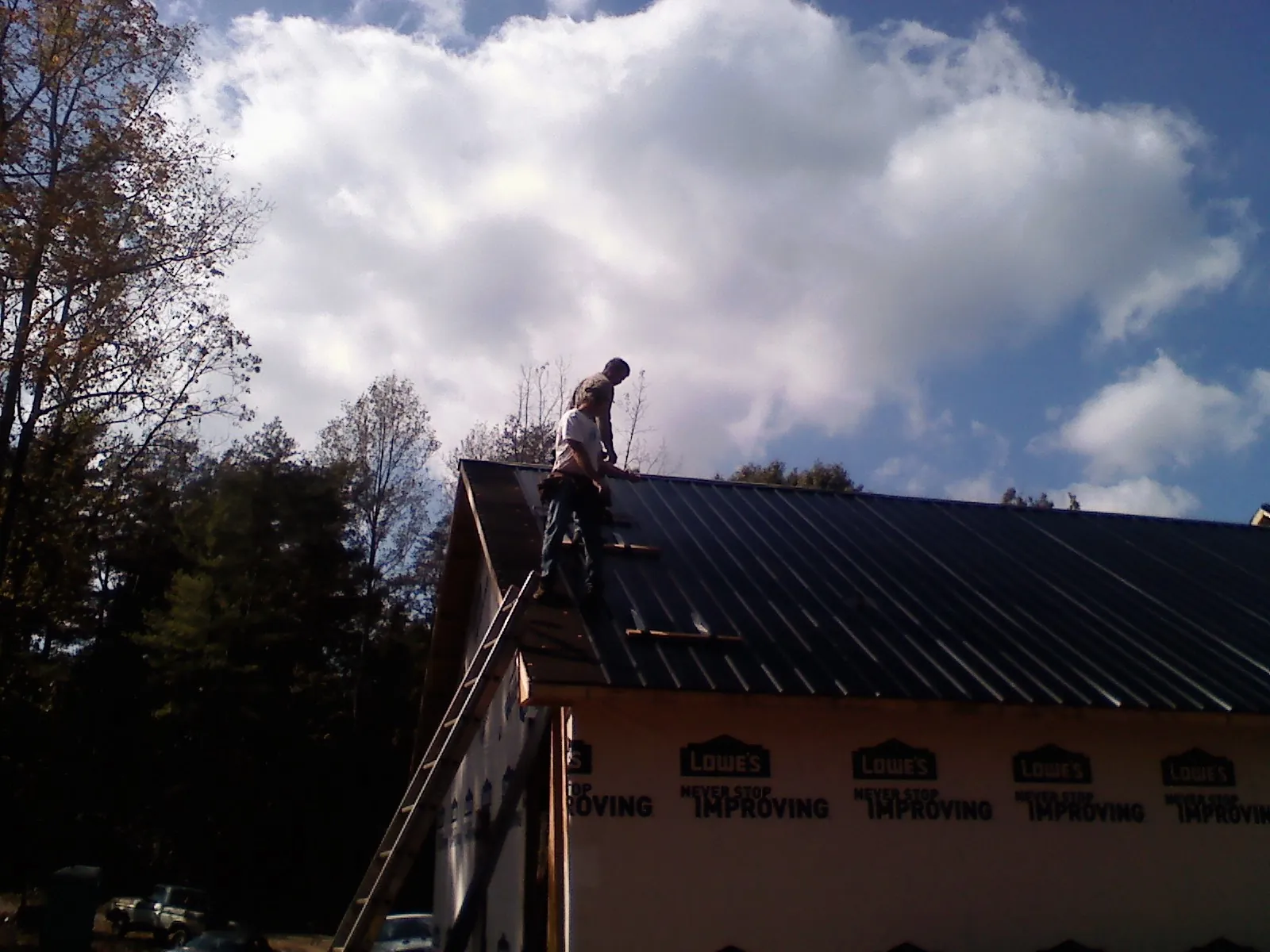 Roofer fastening dark metal panels high against a cloudy sky, from a Roof Inspection job in Warminster