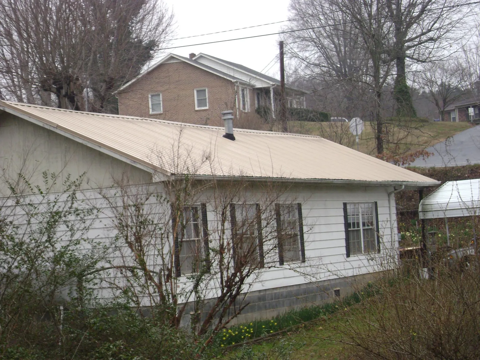 Tan metal roof on a white sided house set into a hillside — Commercial Roofing by Roofing Brothers in Warminster